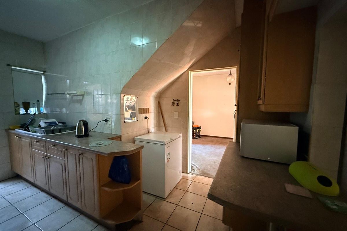 A dated kitchen featuring laminate cabinetry, tiled splashbacks, and ceramic flooring, with an adjacent room visible through the doorway.