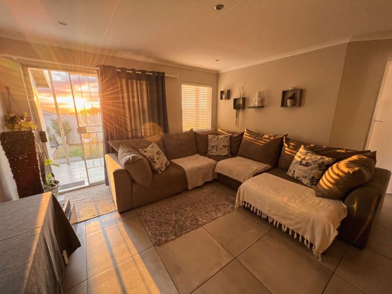 A cozy living room featuring large format floor tiles, recessed lighting, and a sliding glass door that opens to an outdoor patio area.