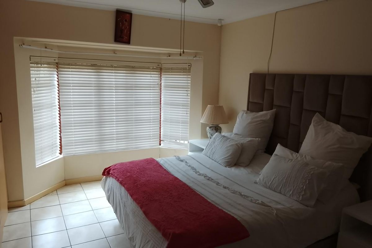 A bedroom featuring a bay window with fitted blinds, tiled flooring, and a ceiling fan.