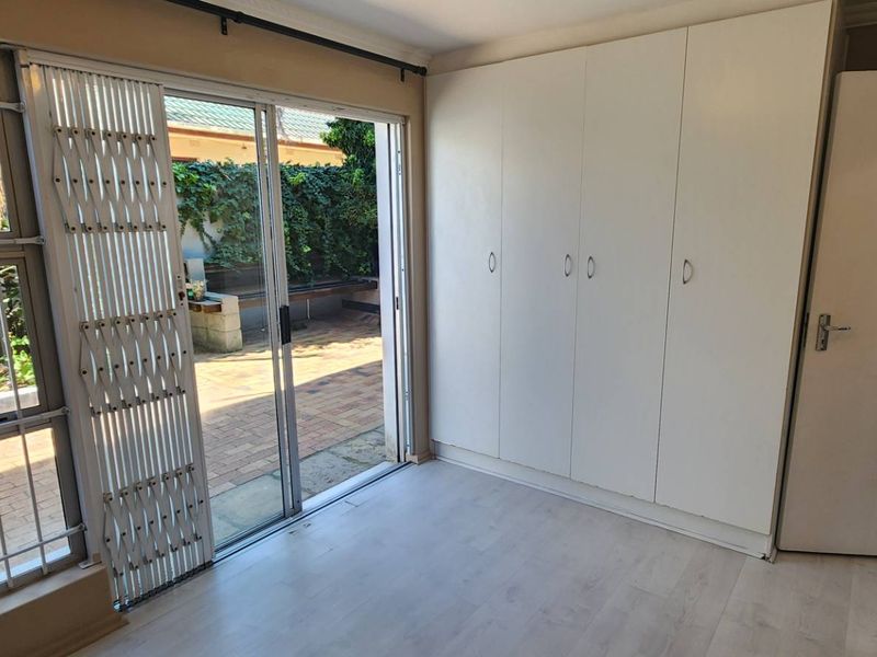 A bright, empty bedroom featuring built-in cupboards, laminate flooring, and a sliding glass door providing direct access to an outdoor patio area.