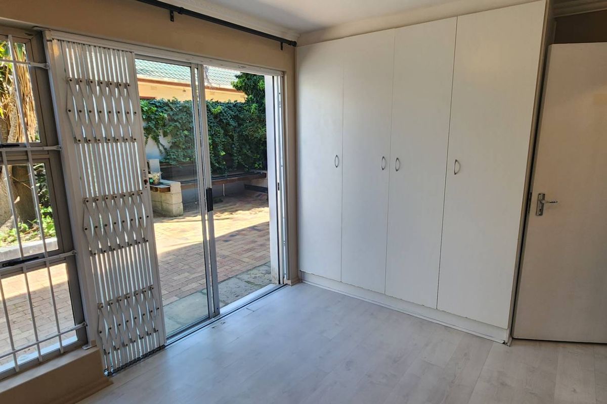 A bright, empty bedroom featuring built-in cupboards, laminate flooring, and a sliding glass door providing direct access to an outdoor patio area.