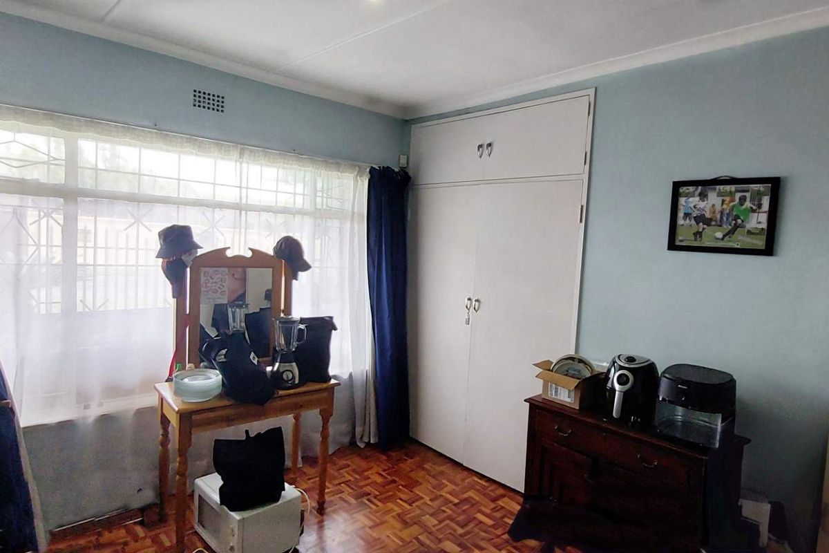 A bedroom featuring parquet flooring, built-in cupboards, and a large window with security bars.