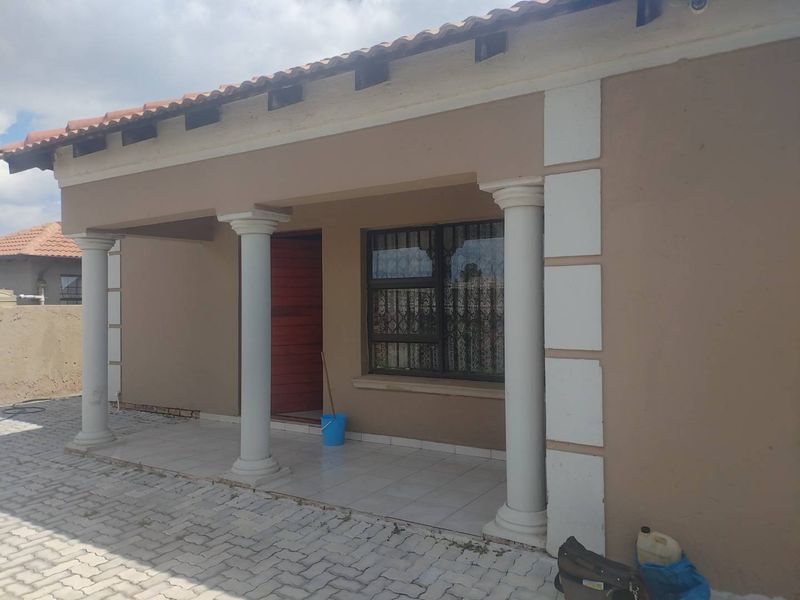 Front entrance of the house featuring a covered patio with decorative columns, tiled flooring, and secure window bars.
