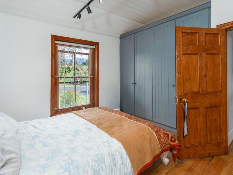 A bedroom featuring timber flooring, built-in blue cabinetry, and a classic timber door with a security gate on the window.