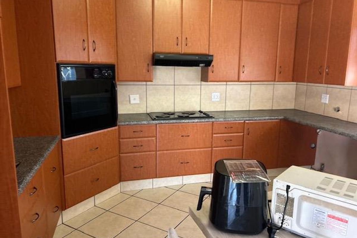 A functional kitchen featuring wood-look cabinetry, granite countertops, a built-in oven, and an electric hob with an extractor fan.