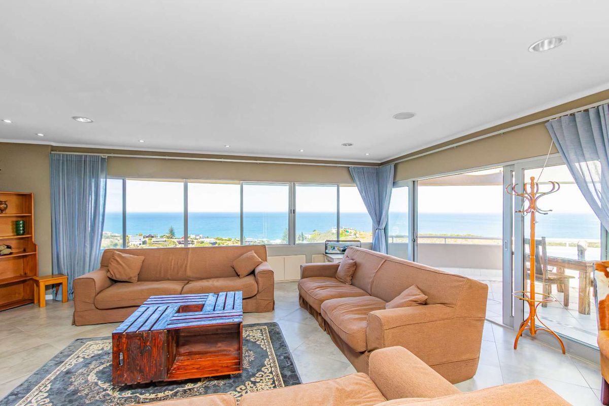 Spacious living area featuring large floor-to-ceiling windows with panoramic ocean views and direct access to an outdoor patio.