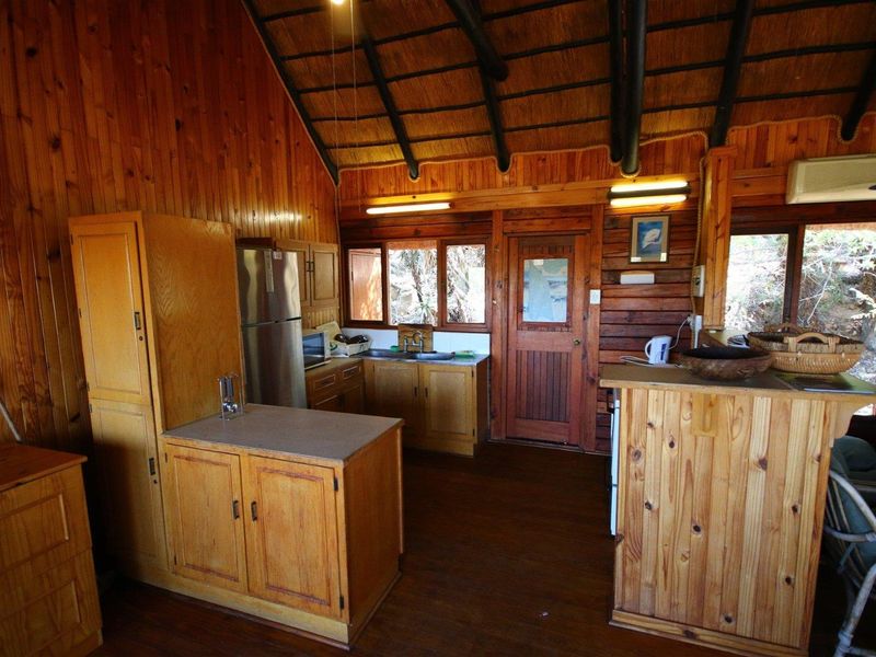 Rustic kitchen featuring extensive timber wall paneling, exposed beam thatched ceiling, built-in wooden cabinetry, and a functional layout with integrated sink and storage.