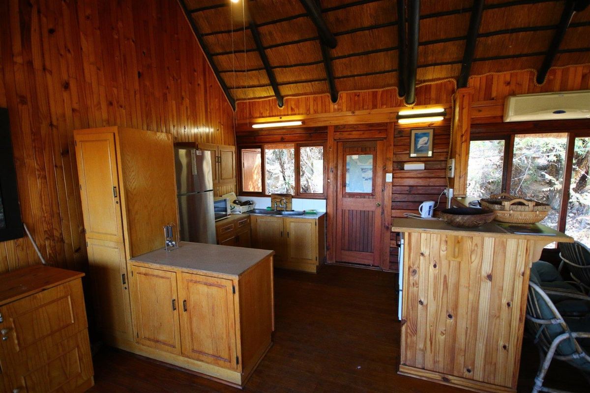 Rustic kitchen featuring extensive timber wall paneling, exposed beam thatched ceiling, built-in wooden cabinetry, and a functional layout with integrated sink and storage.
