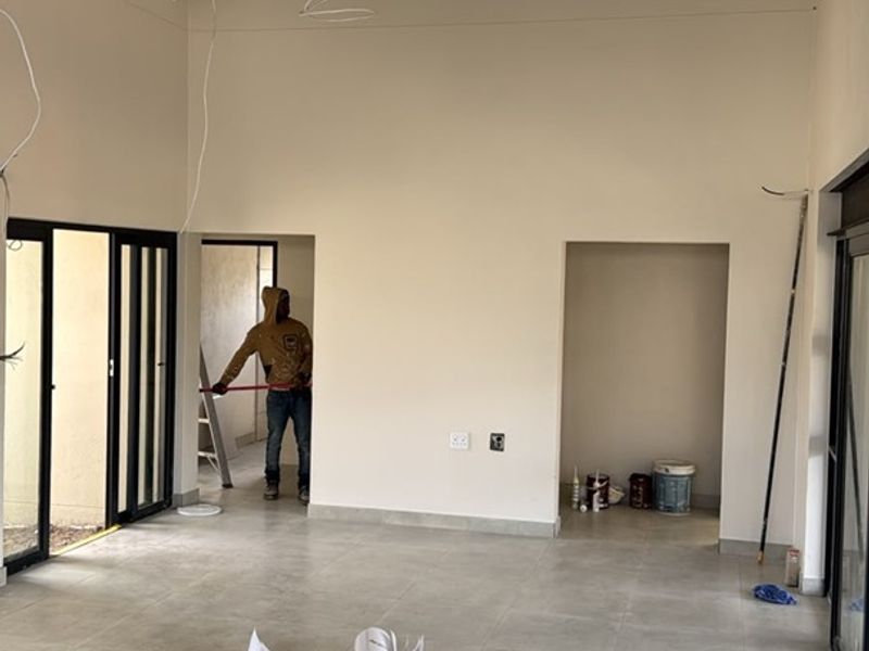 Spacious living area featuring a high vaulted ceiling with exposed trusses, neutral tiled flooring, and large sliding doors providing access to the exterior.