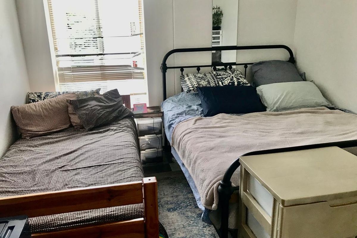 A functional bedroom featuring a window with venetian blinds, providing natural light and a neutral backdrop for potential interior updates.