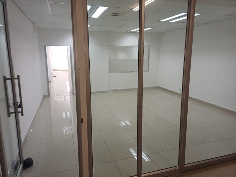 A clean, vacant office space featuring glass partitions, ceramic tiled flooring, and a suspended ceiling with recessed lighting.