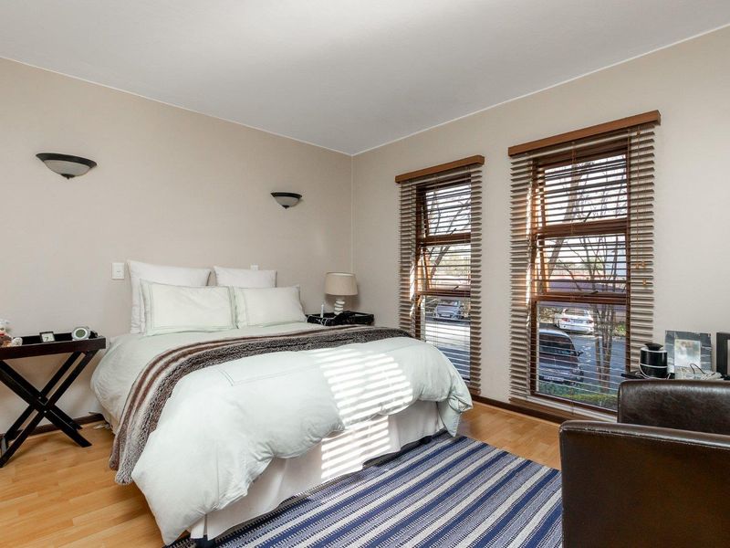 A well-lit bedroom featuring laminate flooring, dual windows with venetian blinds, and wall-mounted lighting fixtures.