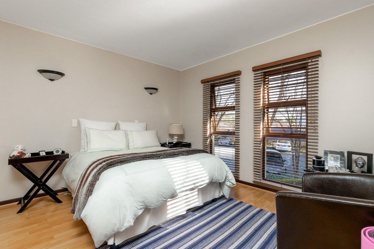 A well-lit bedroom featuring laminate flooring, dual windows with venetian blinds, and wall-mounted lighting fixtures.
