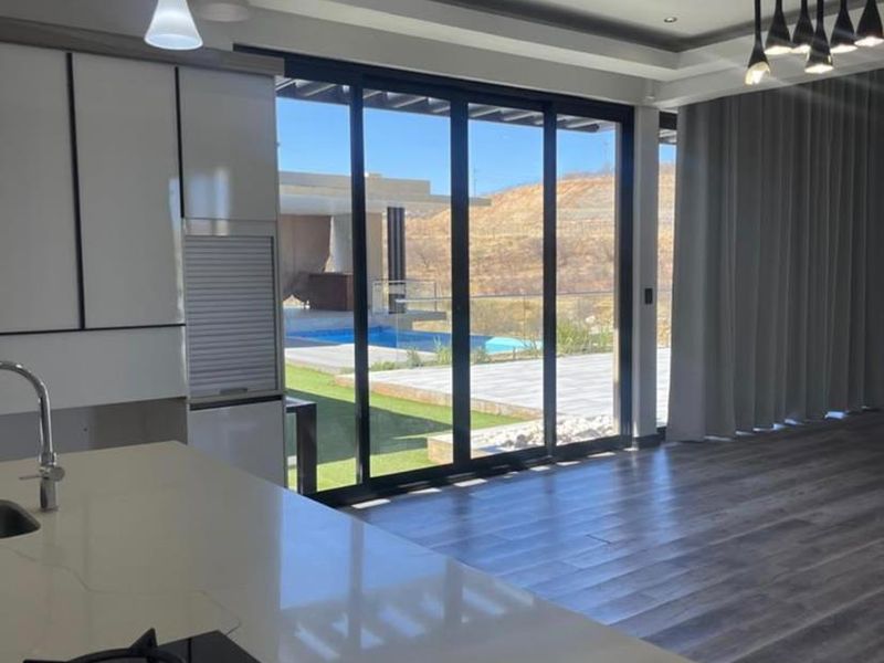 Modern open-plan kitchen and living area featuring sleek cabinetry, gas hob, and large sliding doors opening to a pool and patio area.