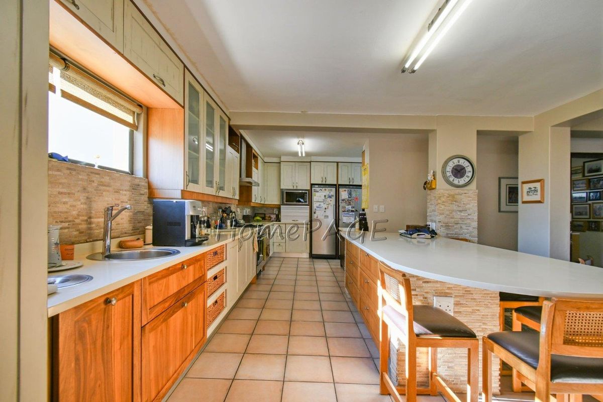 Spacious kitchen featuring extensive wooden cabinetry, stone-tiled backsplash, integrated breakfast bar, and tiled flooring, offering ample storage and prep space.