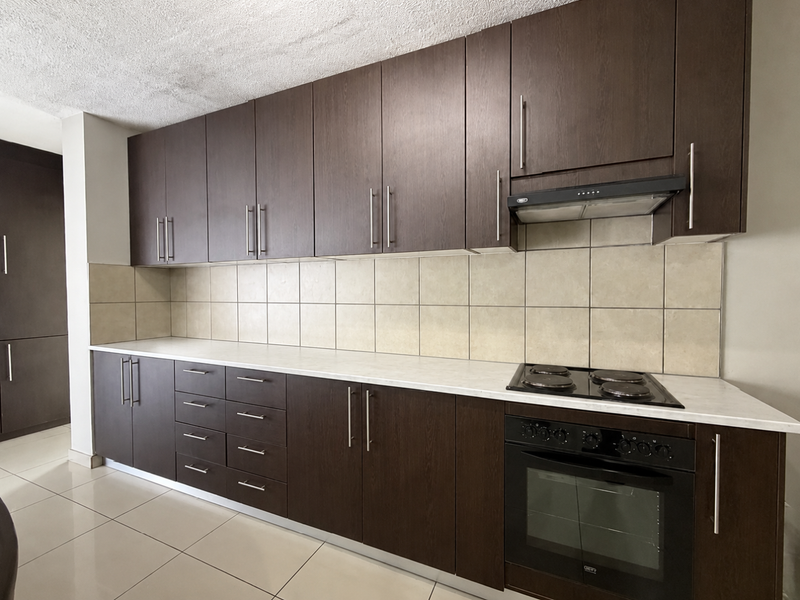 A functional kitchen featuring dark wood cabinetry, light laminate countertops, a built-in oven with hob, and neutral ceramic tile backsplash.