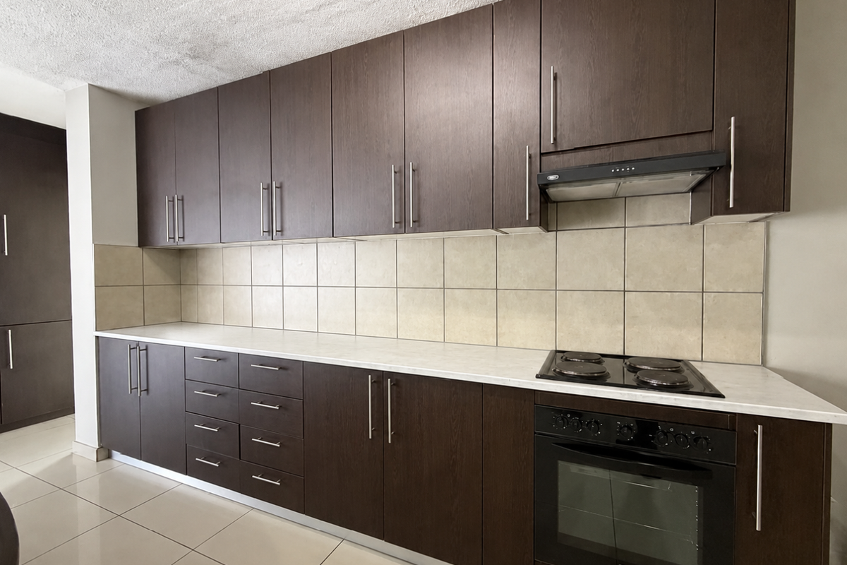 A functional kitchen featuring dark wood cabinetry, light laminate countertops, a built-in oven with hob, and neutral ceramic tile backsplash.