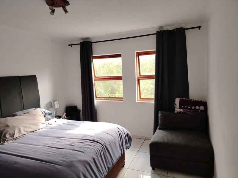 A bedroom featuring tiled flooring, timber-framed windows, and neutral wall finishes, providing a functional and well-lit sleeping space.
