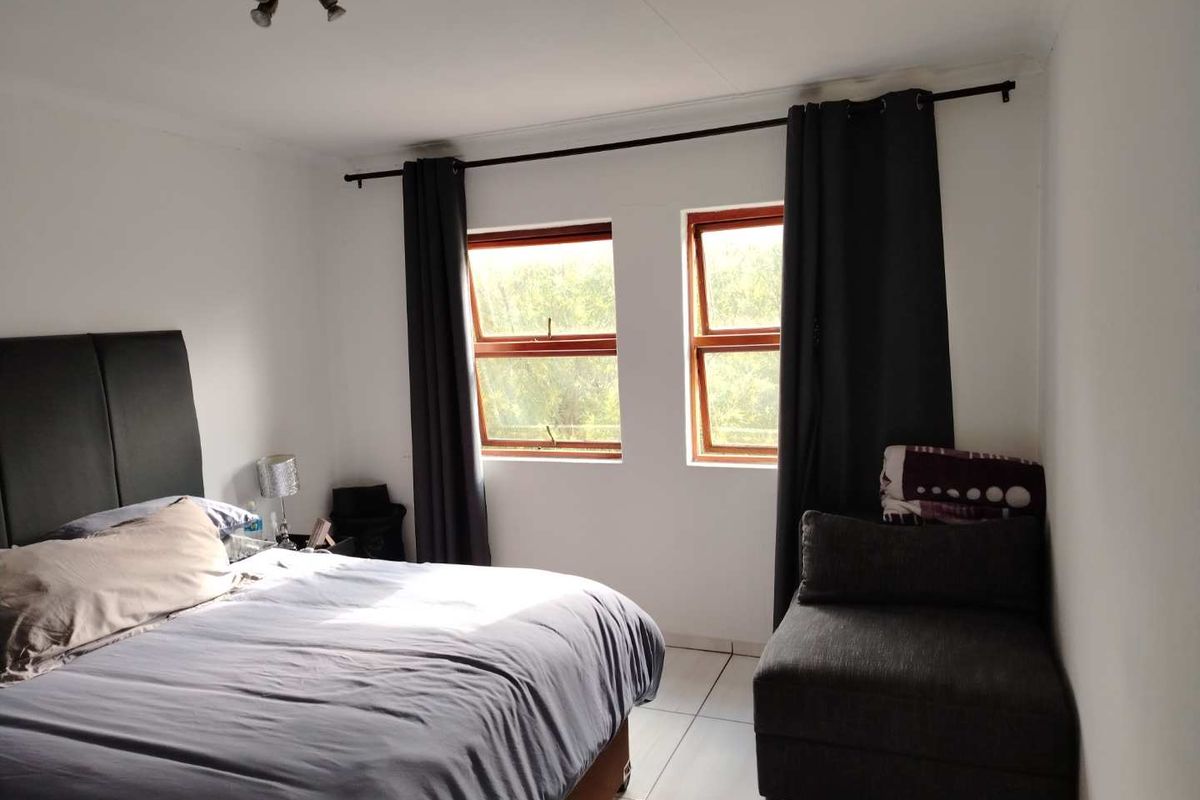 A bedroom featuring tiled flooring, timber-framed windows, and neutral wall finishes, providing a functional and well-lit sleeping space.
