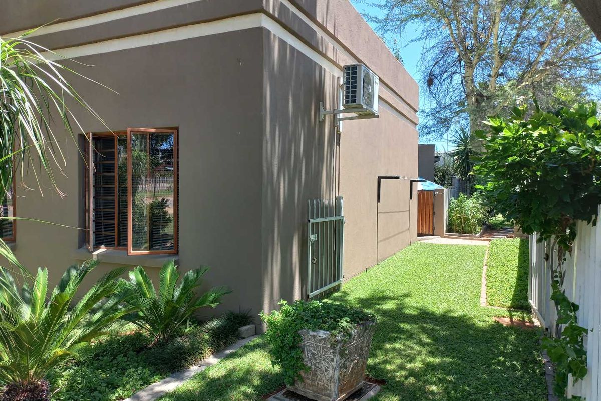A well-maintained side garden area featuring a manicured lawn, established landscaping, and a wall-mounted air conditioning unit.
