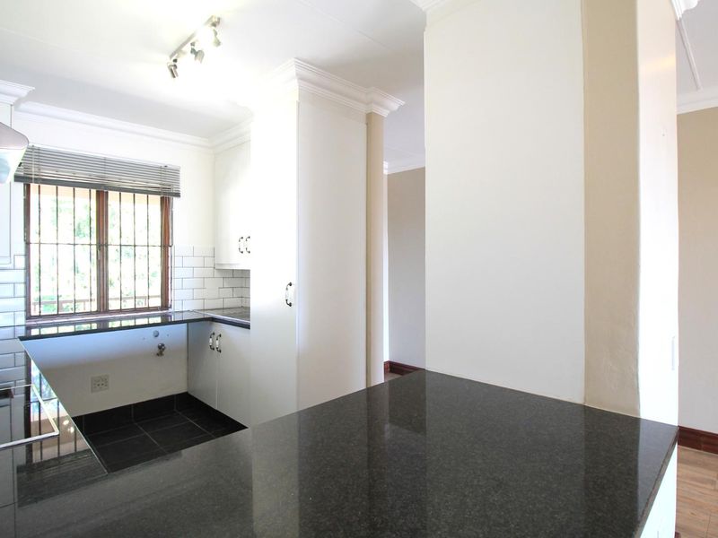Modern kitchen featuring dark granite countertops, white cabinetry, subway tile backsplash, and stainless steel extractor fan with ample natural light.