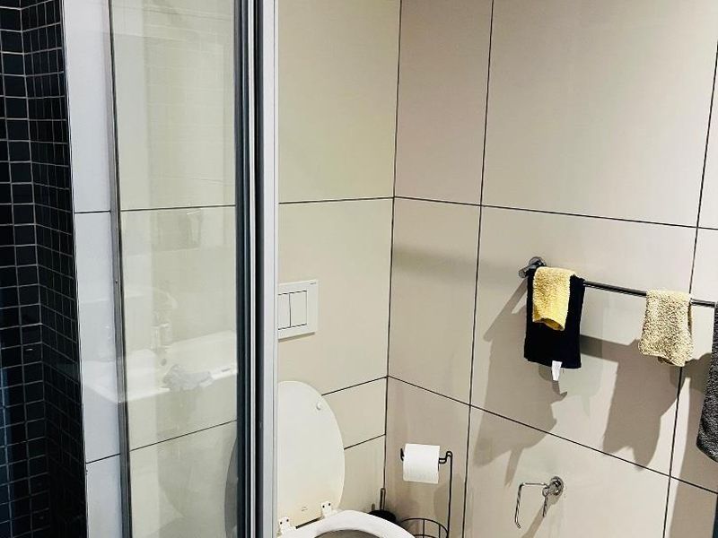 A modern bathroom featuring a glass-enclosed shower, neutral wall tiling, and a wall-mounted toilet with integrated flush system.