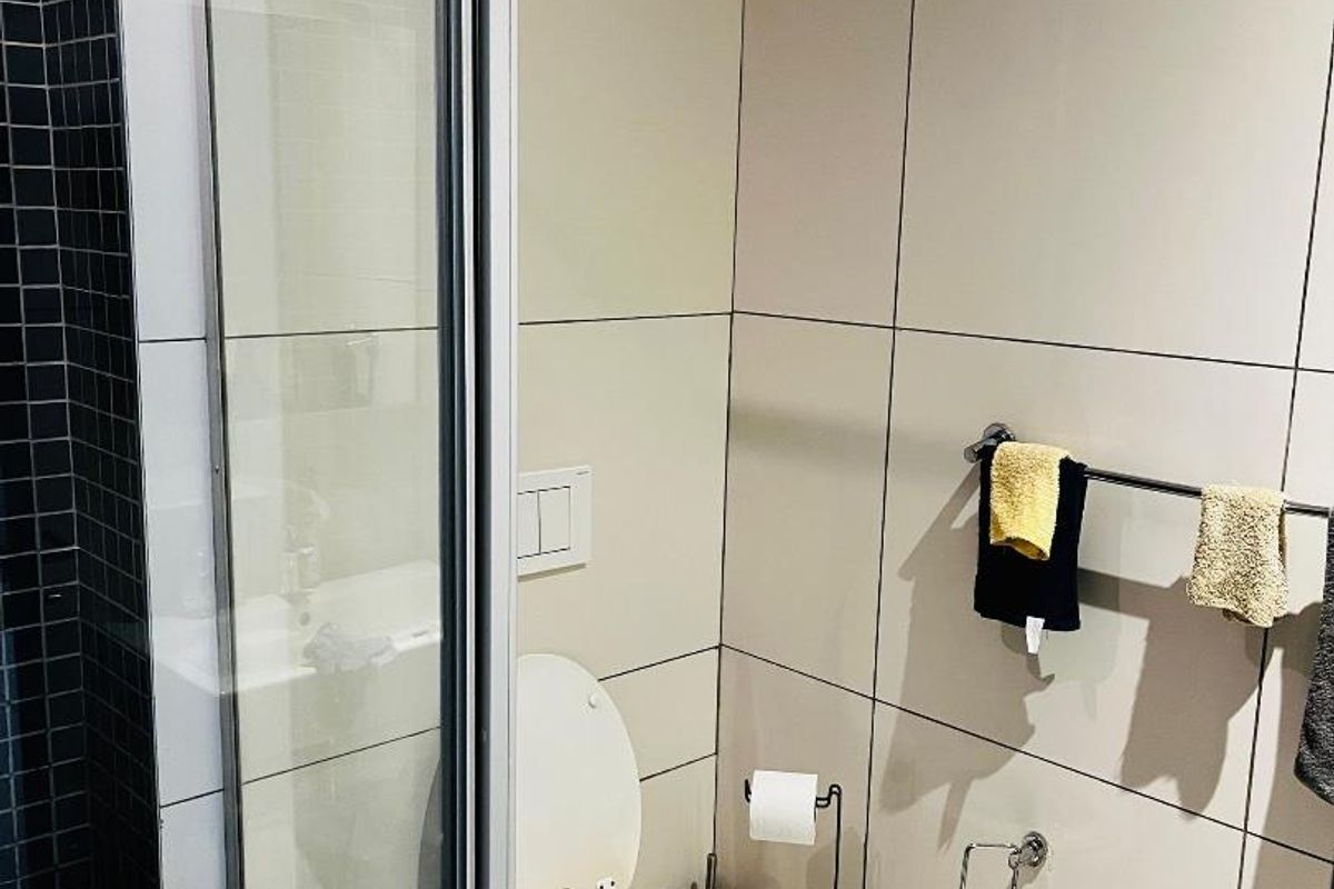 A modern bathroom featuring a glass-enclosed shower, neutral wall tiling, and a wall-mounted toilet with integrated flush system.