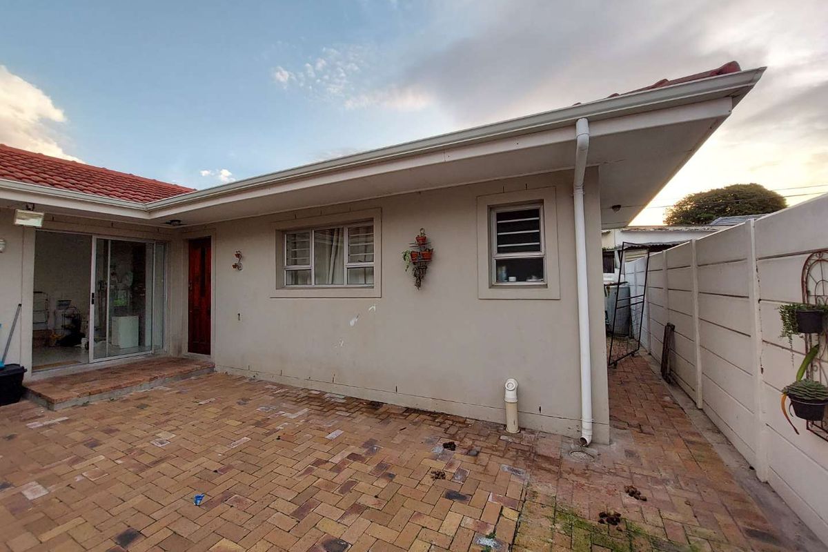 Rear exterior view of the apartment featuring a paved courtyard, sliding glass door access, and a perimeter boundary wall.
