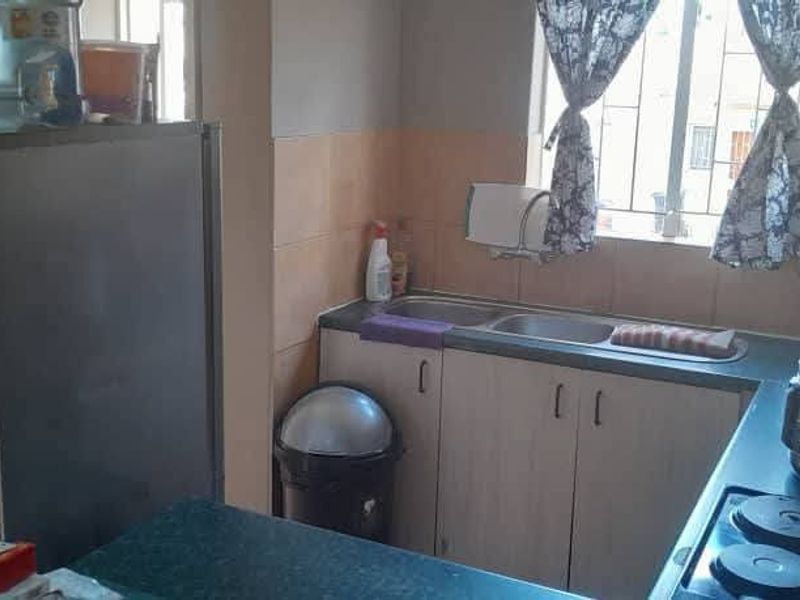 A functional kitchen featuring built-in cabinetry, laminate countertops, a double bowl sink, and a tiled splashback with security bars on the window.