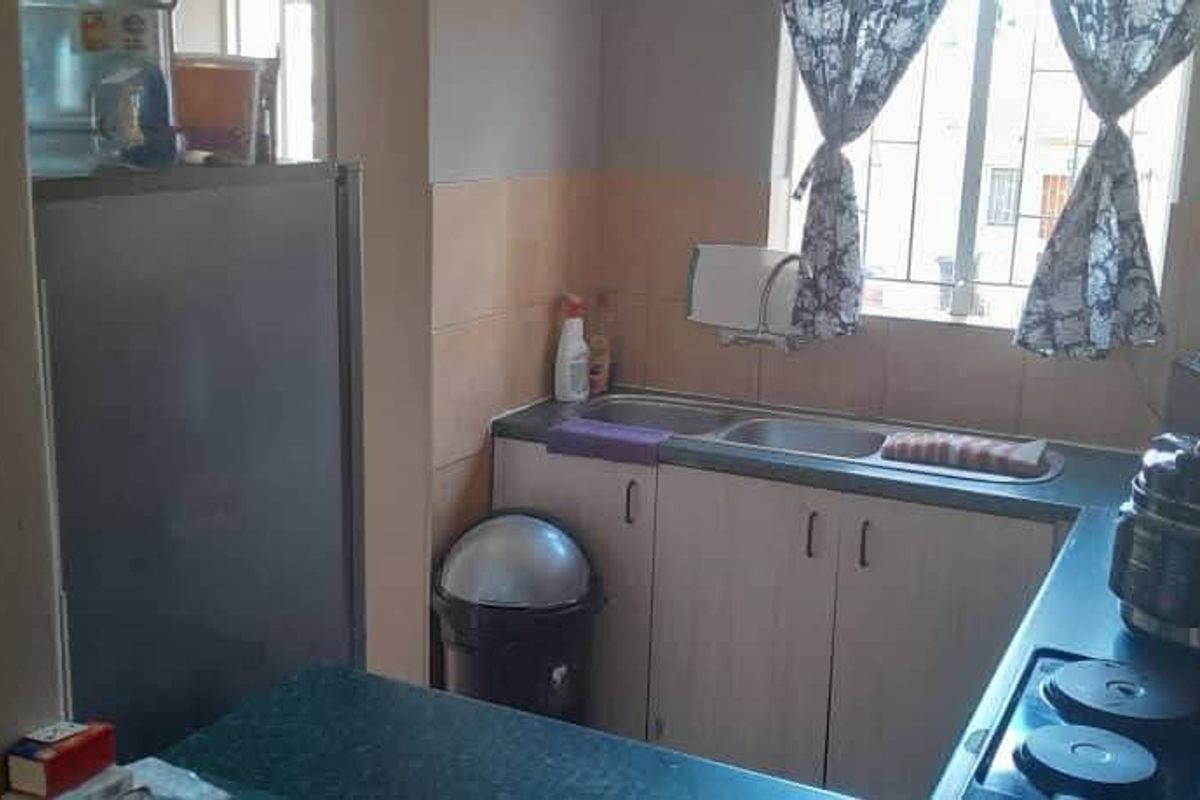 A functional kitchen featuring built-in cabinetry, laminate countertops, a double bowl sink, and a tiled splashback with security bars on the window.