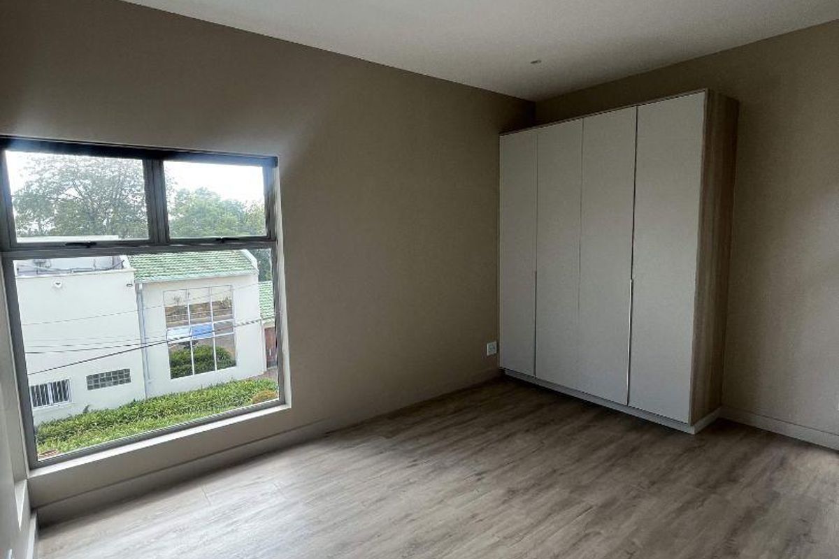 A bright, modern bedroom featuring light wood-look laminate flooring, neutral wall tones, and built-in floor-to-ceiling cabinetry.
