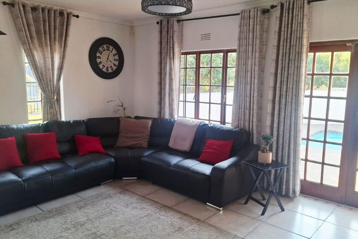 A comfortable living room featuring tiled flooring, wooden window frames, and french doors providing direct access to the outdoor pool area.