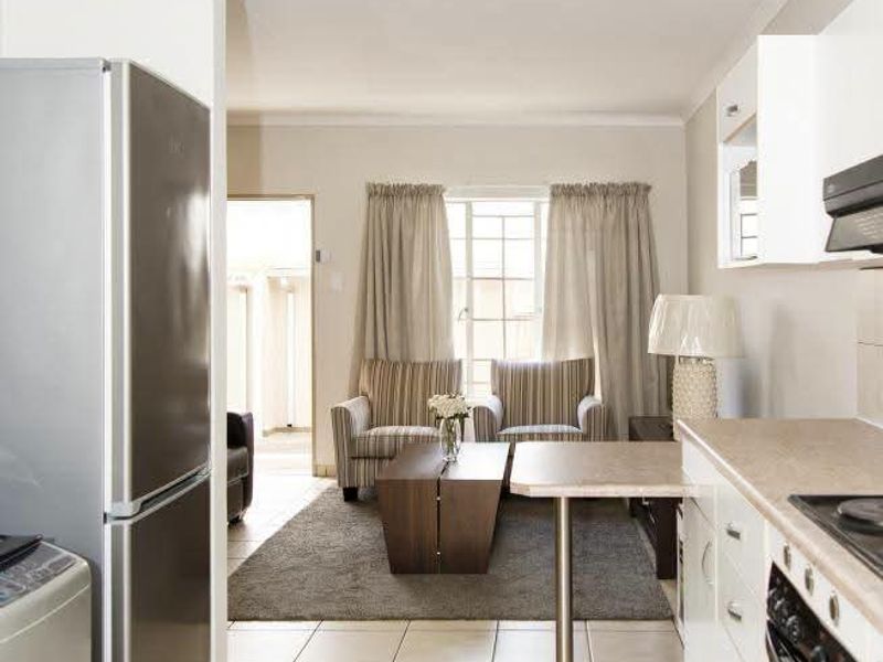 Open-plan kitchen and living area featuring tiled flooring, built-in cabinetry, and integrated cooking appliances, leading to a bright lounge space.