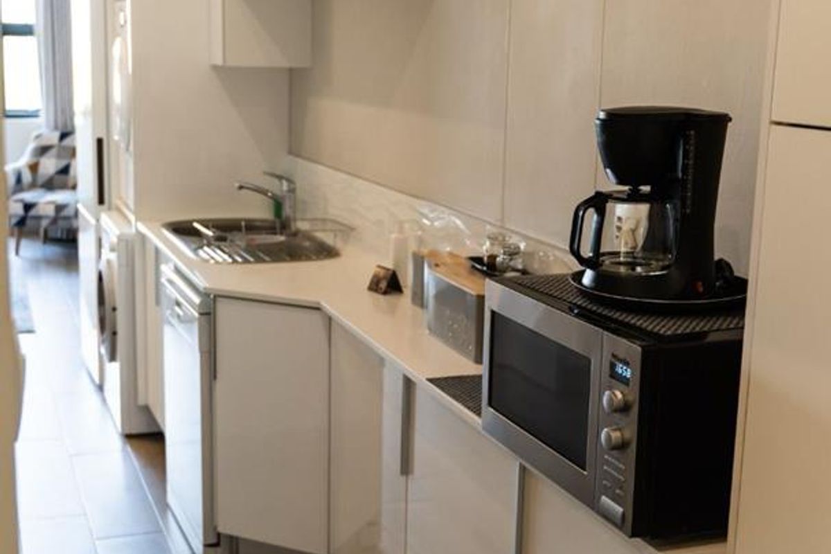 A modern, compact galley-style kitchen featuring sleek white cabinetry, integrated appliances, and wood-look tiled flooring.