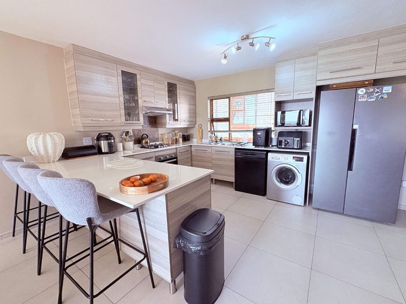 Modern kitchen featuring light wood-grain cabinetry, stone countertops, a breakfast bar, and integrated appliances, finished with neutral floor tiles.