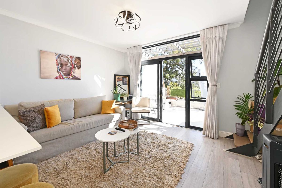 Bright living room featuring light wood-look flooring, modern ceiling lighting, and large sliding glass doors providing seamless access to an outdoor patio area.