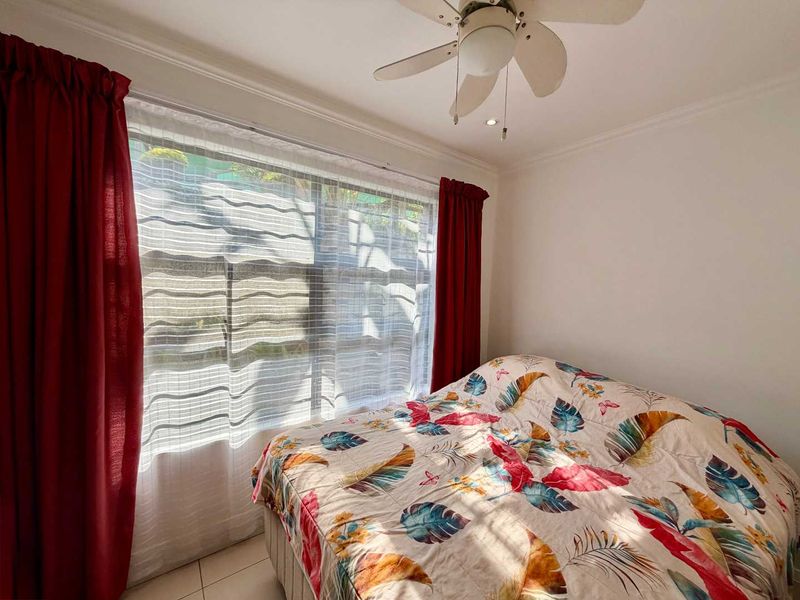 A bedroom featuring tiled flooring and a ceiling fan, with natural light entering through a large window.