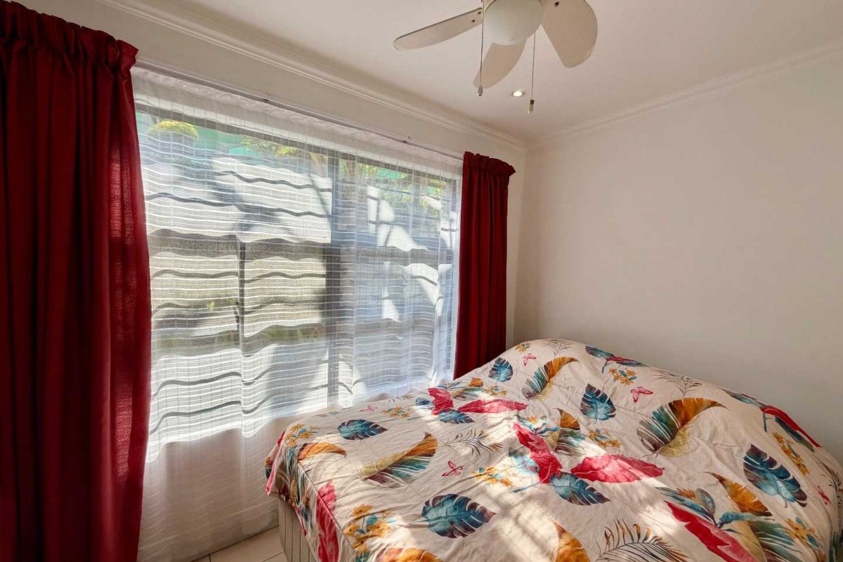 A bedroom featuring tiled flooring and a ceiling fan, with natural light entering through a large window.