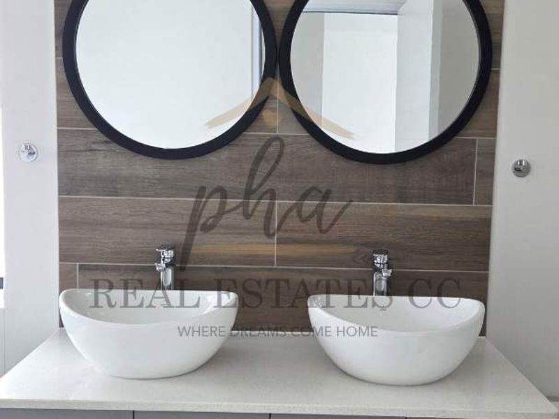 Modern bathroom vanity featuring a double vessel sink setup, stone countertop, grey cabinetry, and a stylish wood-look tiled feature wall.