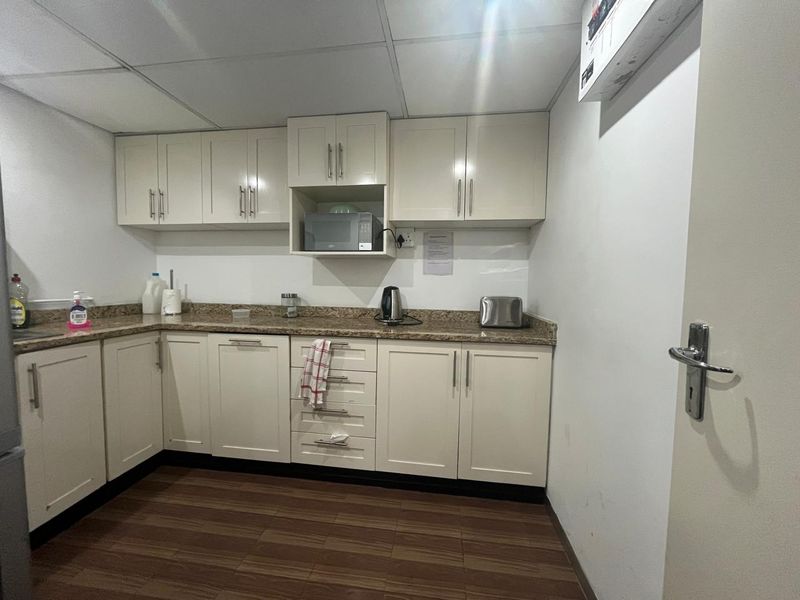 A functional office kitchenette featuring cream-colored cabinetry, granite countertops, and a drop ceiling with an integrated air conditioning unit.