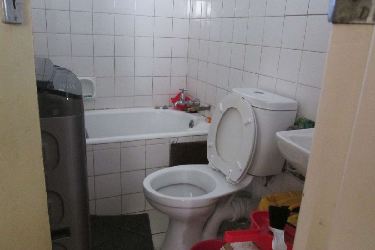 A compact bathroom featuring a bathtub, toilet, and washbasin with white wall tiling. The space requires cosmetic updates to improve its overall condition.