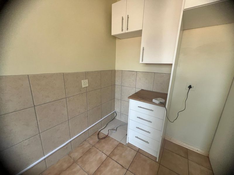 A compact kitchen area featuring built-in white cabinetry, tiled splashbacks, and tiled flooring, currently vacant and ready for appliance installation.