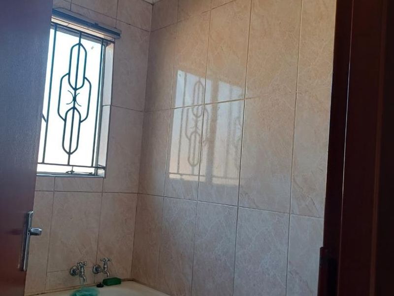 A functional bathroom featuring a built-in bathtub, wall-mounted faucet, and full-height ceramic wall tiling with decorative ceiling cornicing.