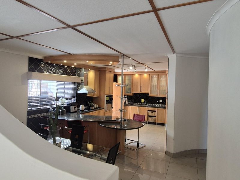 A functional kitchen featuring wooden cabinetry, a central island with breakfast bar, tiled flooring, and a dark tiled backsplash.