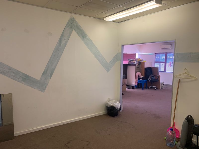 Office space featuring a suspended ceiling, fluorescent lighting, and an air conditioning unit, with visible wear to the carpet and wall finishes.