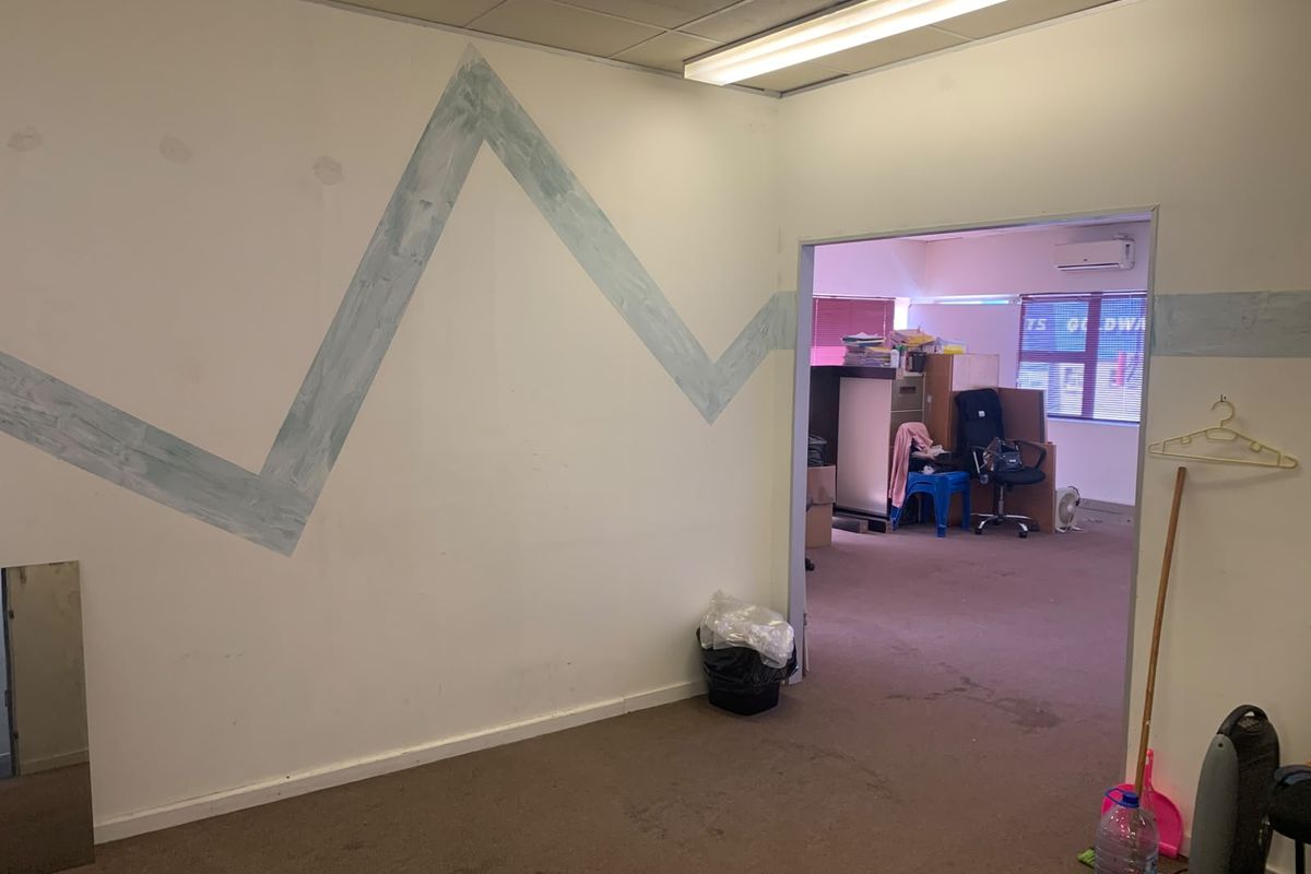 Office space featuring a suspended ceiling, fluorescent lighting, and an air conditioning unit, with visible wear to the carpet and wall finishes.