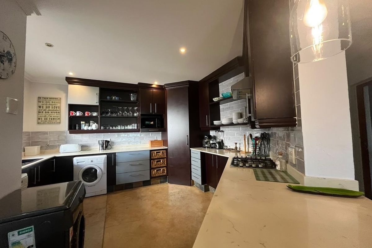 A well-appointed kitchen featuring dark cabinetry, stone countertops, a gas hob with extractor, and a subway tile backsplash with integrated appliances.