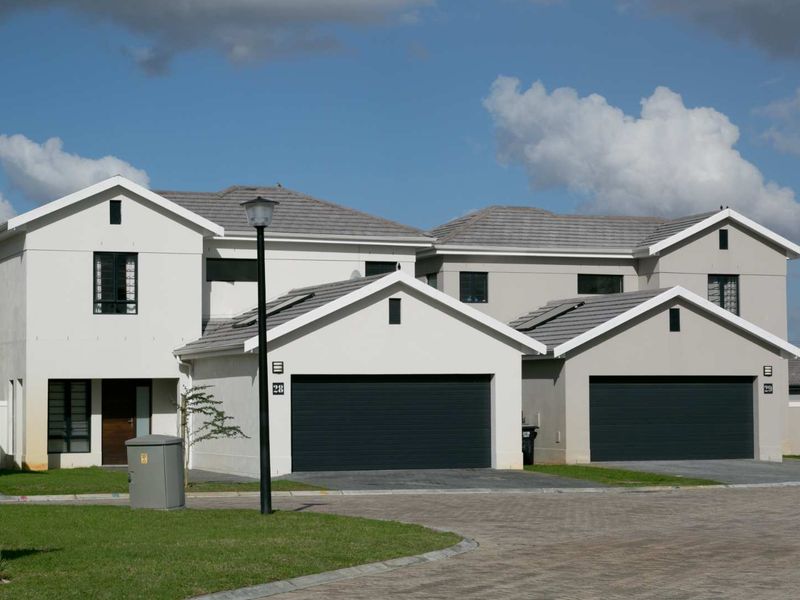 Front elevation of a modern townhouse complex featuring double garages, tiled roofing, and paved driveway access.