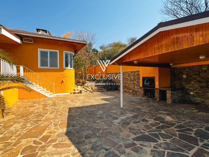 Spacious outdoor entertainment area featuring a covered patio with a built-in braai, stone paving, and attractive stone cladding accents.