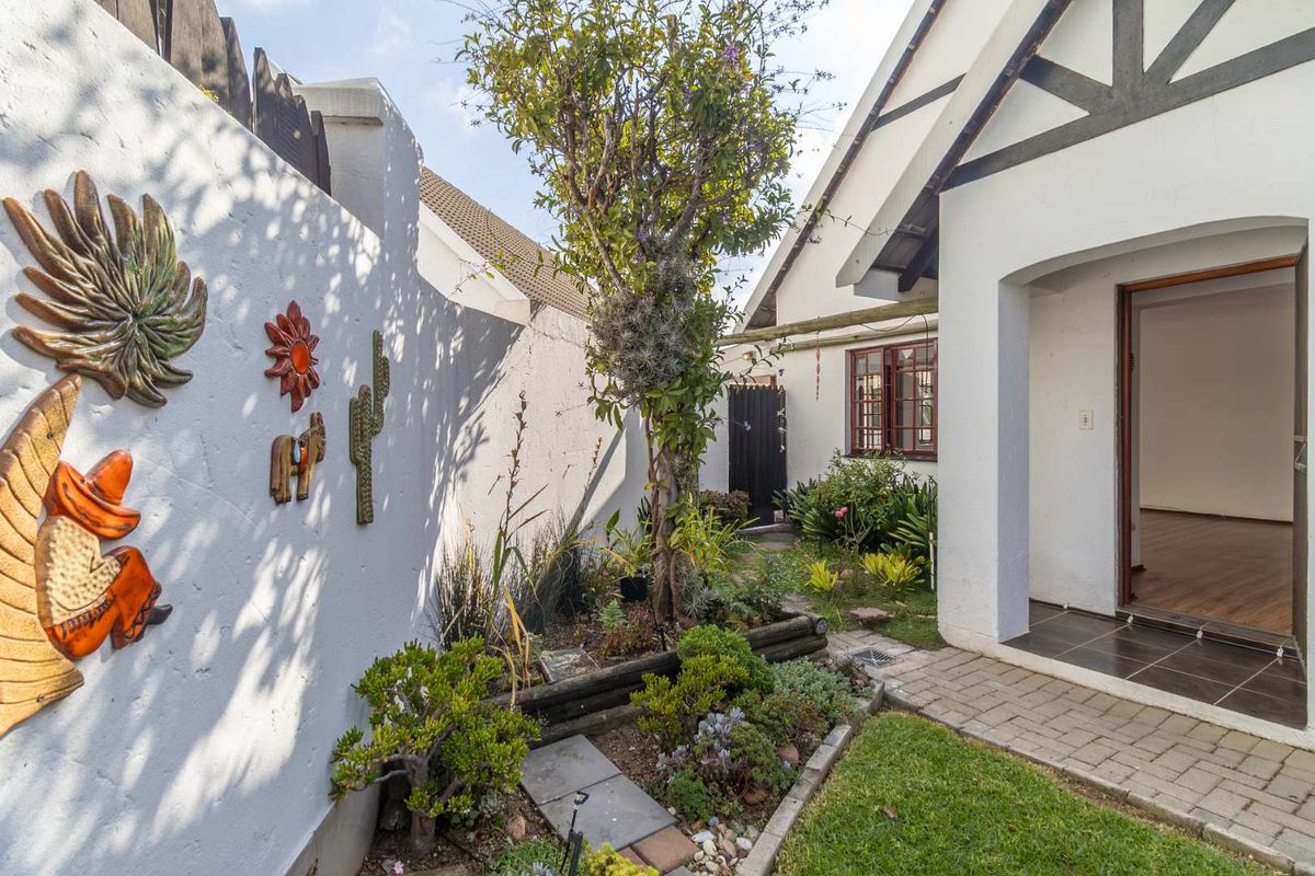 A well-maintained rear garden area featuring a paved walkway leading to the home entrance, bordered by a white boundary wall and established garden beds.